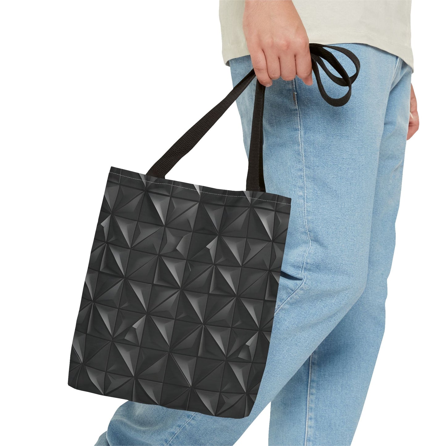 A man holds in his right hand a tote bag with a matte black base embossed with a 3D pyramid tile pattern, with the vertices of each triangle repeating.