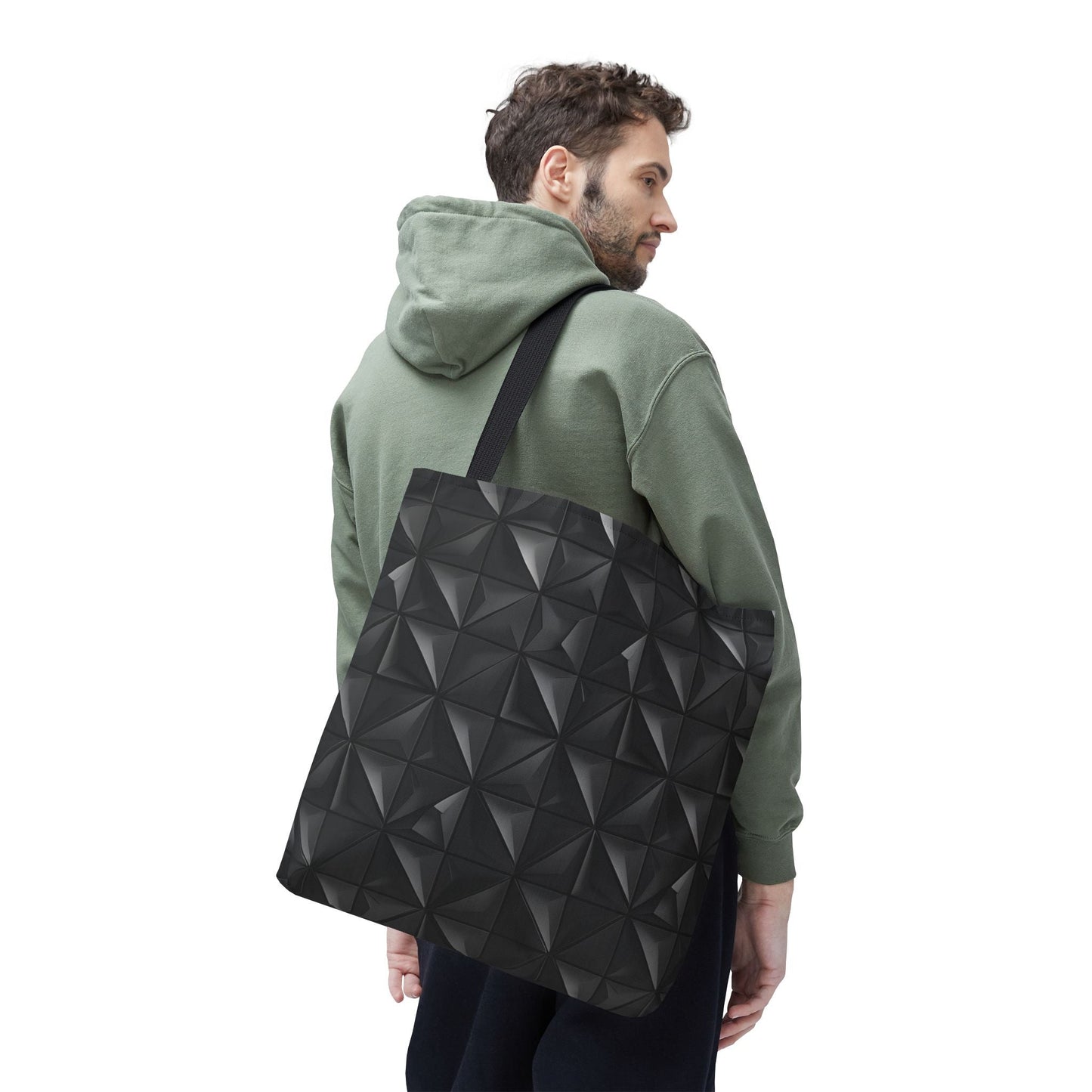 A man is wearing a tote bag with a matte black base embossed with a 3D pyramid tile pattern, with the vertices of each triangle repeating, over his right shoulder, looking diagonally back.