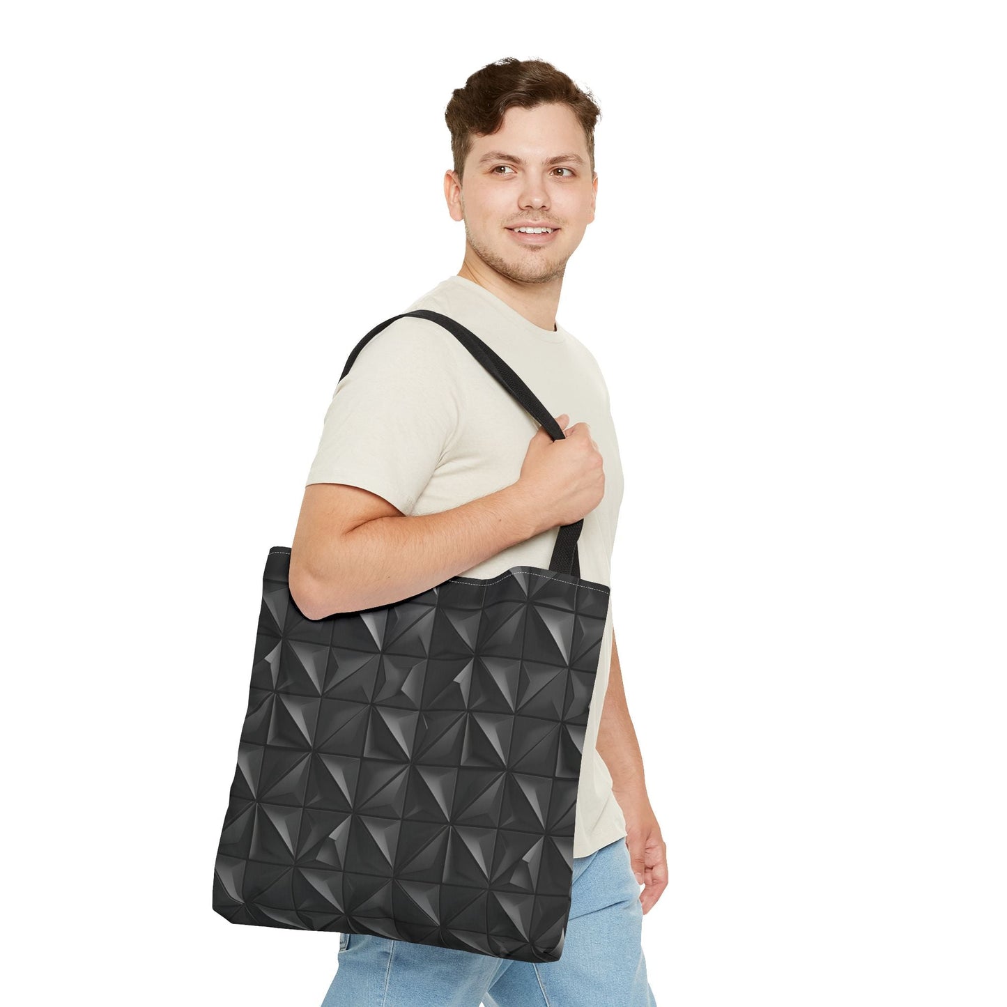A man slings over his right shoulder a tote bag with a matte black base embossed with a 3D pyramid tile pattern, with the vertices of each triangle repeating.