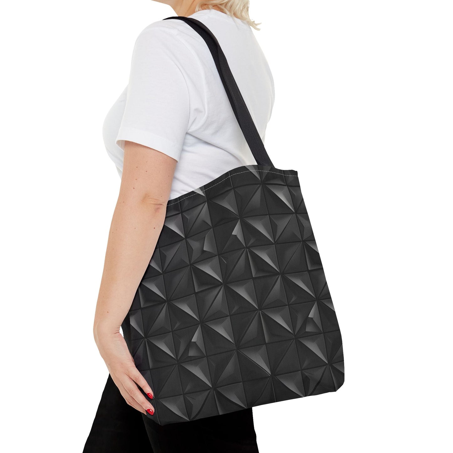 A woman is wearing a tote bag with a matte black base embossed with a 3D pyramid tile pattern, with the vertices of each triangle repeating over her left shoulder.