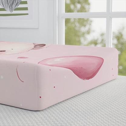 A half-view of the baby changing pad cover featuring an adorable pink bear, with a soft pink background adorned with balloons, gift boxes, and heart motifs.