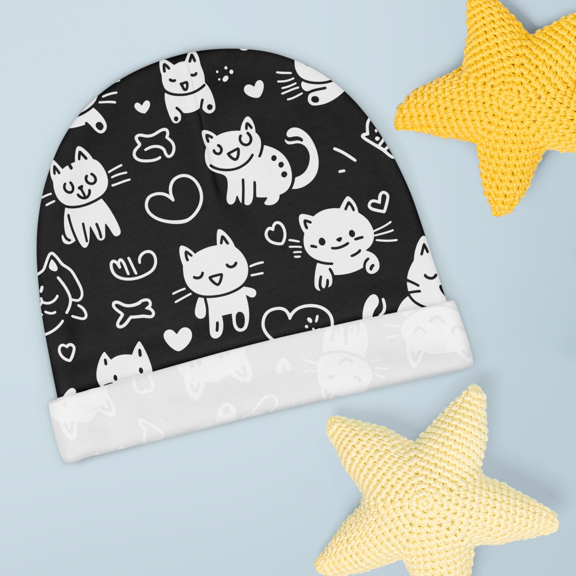 The cuff of this adorable baby beanie, featuring a playful cat pattern, is folded over.