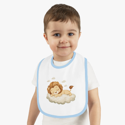 A baby boy wearing an adorable bib with a light blue-colored trim and a white base, featuring a design of a cute lion peacefully sleeping on a fluffy cloud.