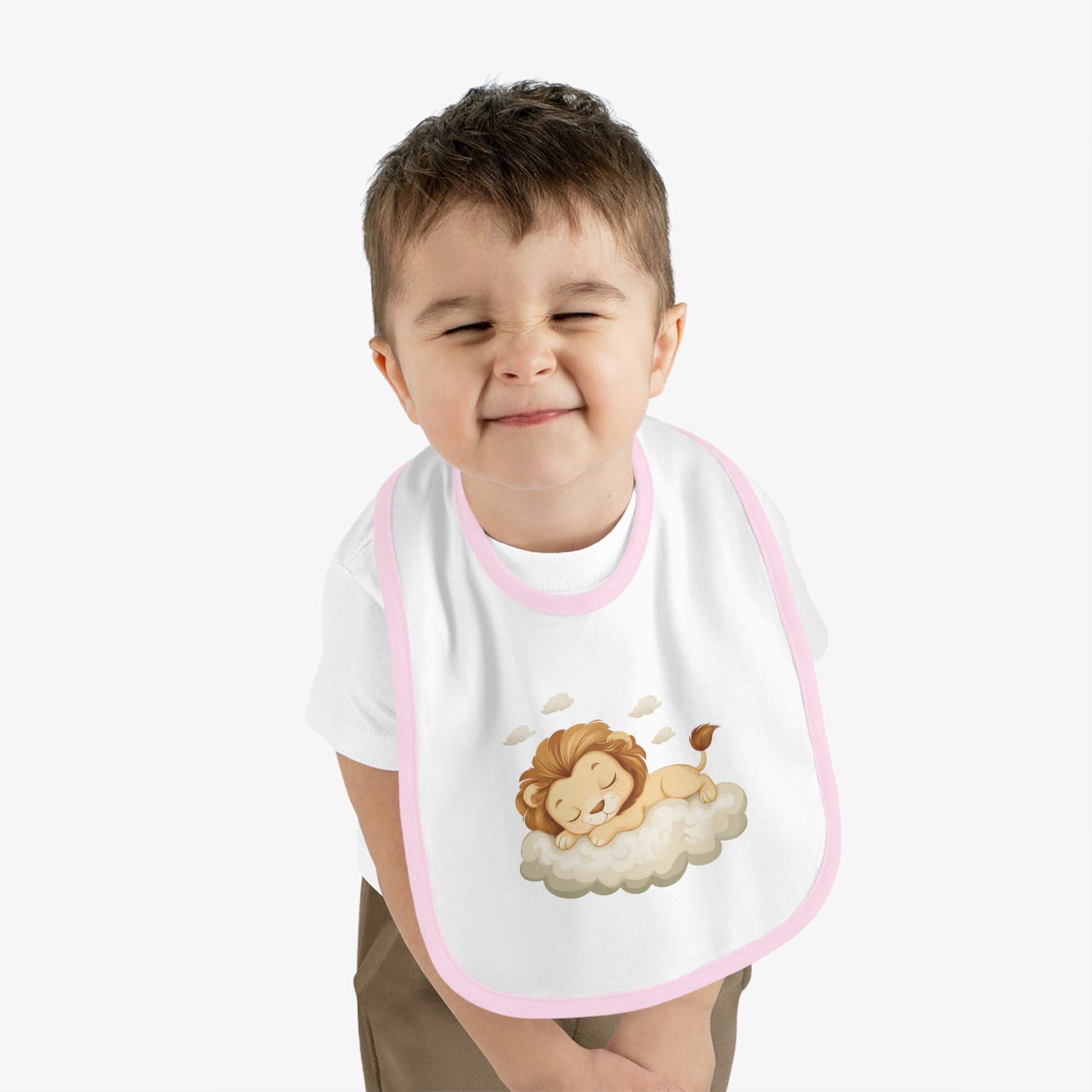 A baby boy wearing an adorable bib with a pink-colored trim and a white base, featuring a design of a cute lion peacefully sleeping on a fluffy cloud.