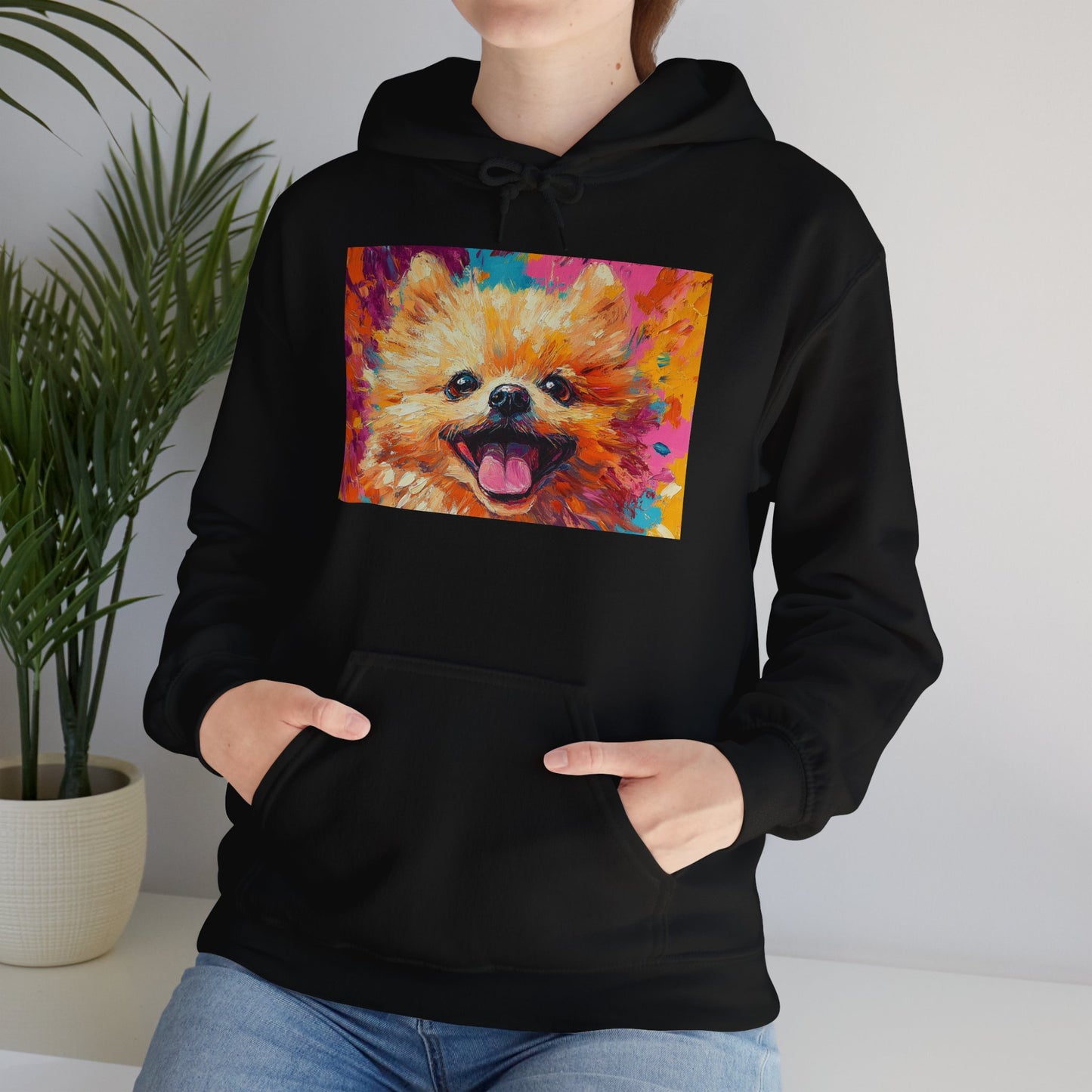 A woman wearing a Black hoodie with a vivid acrylic-style artwork of a Pomeranian dog, with both hands in her pockets.
