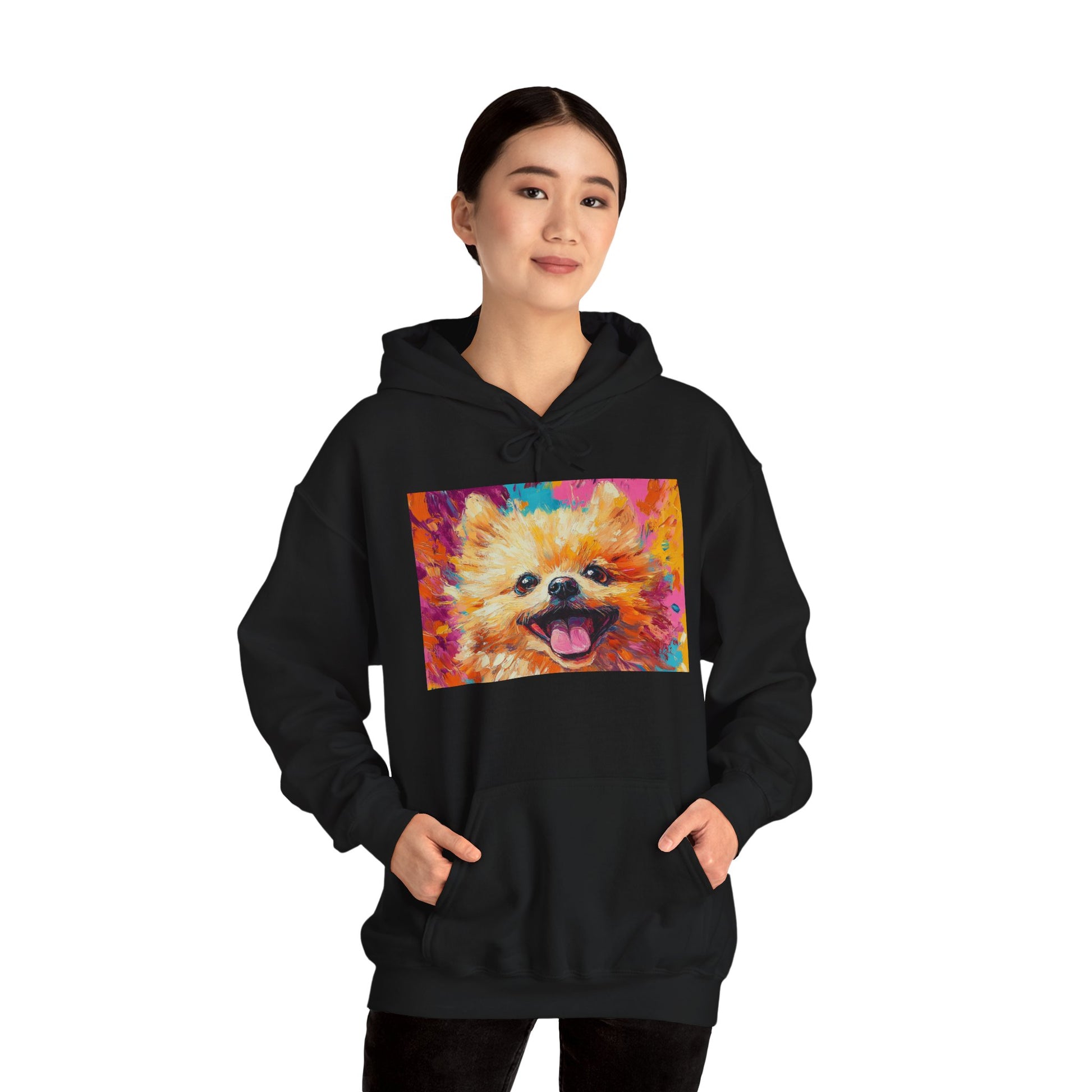 A woman standing with both hands in her pockets, wearing a Black hoodie with a vivid acrylic-style artwork of a Pomeranian dog.
