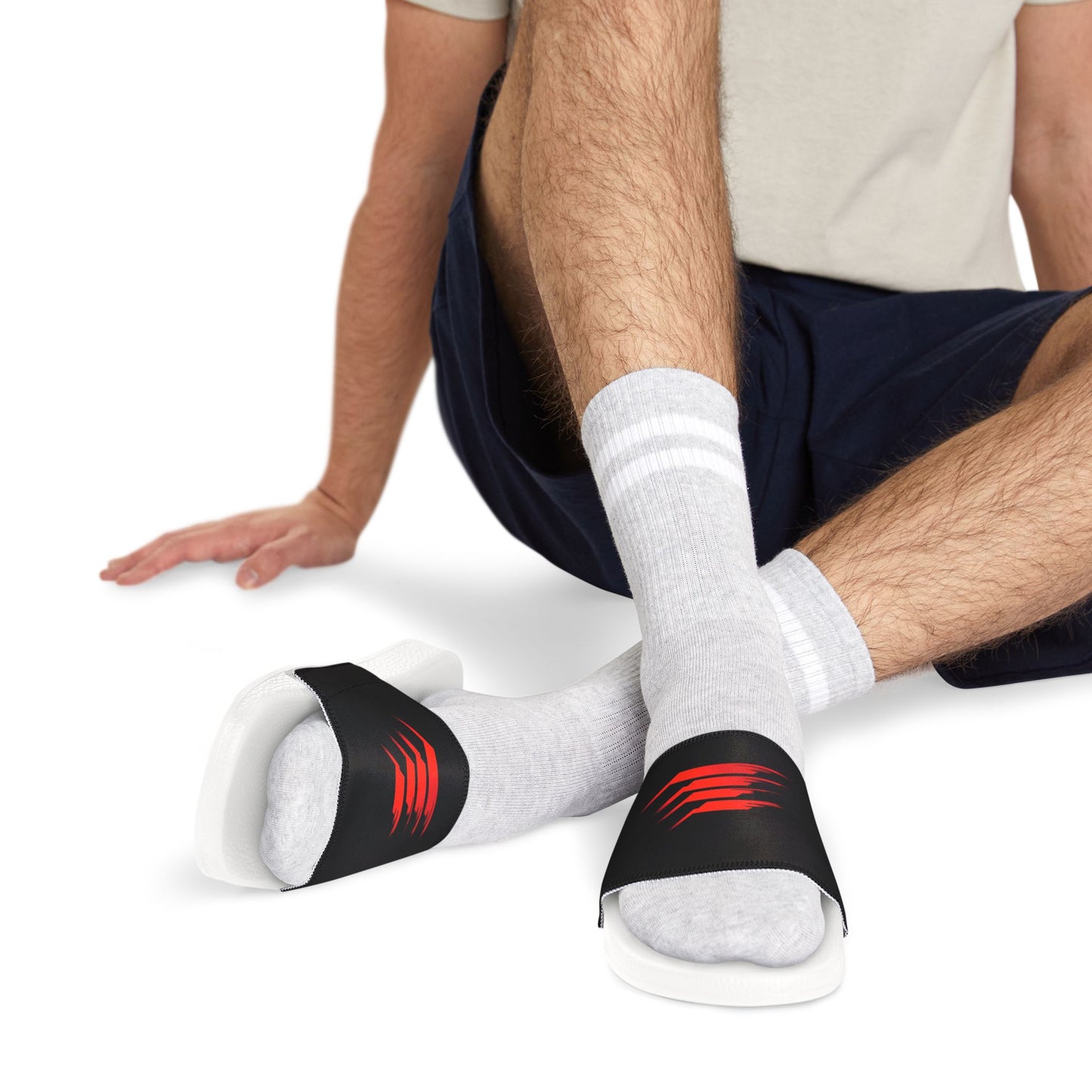 A seated man wearing these sandals featuring a bold red and black graphic design.