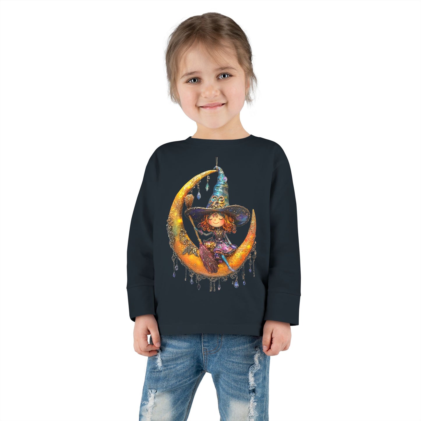 A young girl wearing a Black long-sleeve T-shirt featuring a whimsical design of a small witch sitting on a large moon adorned with scattered crystals.