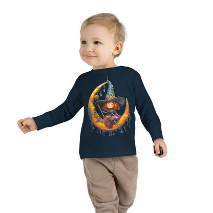 A young boy wearing a Navy long-sleeve T-shirt featuring a whimsical design of a small witch sitting on a large moon adorned with scattered crystals.