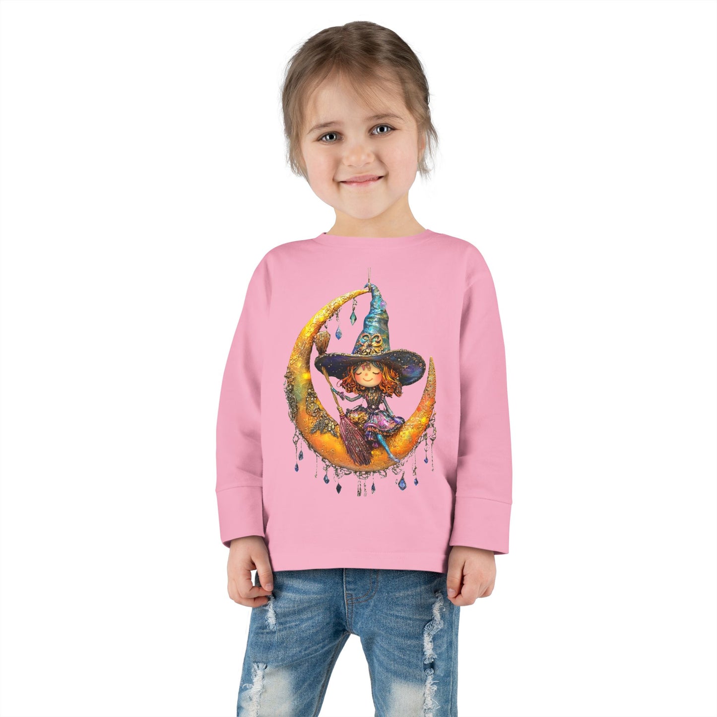 A young girl wearing a Pink long-sleeve T-shirt featuring a whimsical design of a small witch sitting on a large moon adorned with scattered crystals.