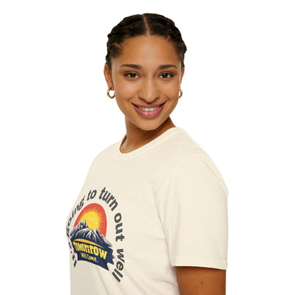 A woman looking forward while wearing a natural-colored T-shirt designed with an uplifting message and a warm sunrise graphic.